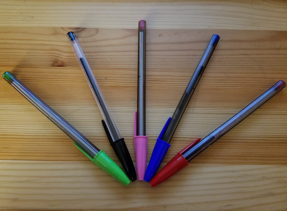 5 Bic pens fanned out. Green, black, pink, blue, and red.
